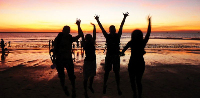 four friends on a beach in darwin with the sun setting in the background