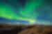 Green waves of the Northern Lights undulate over the rocky mountainous landscape of Thingvellir National Park, Iceland