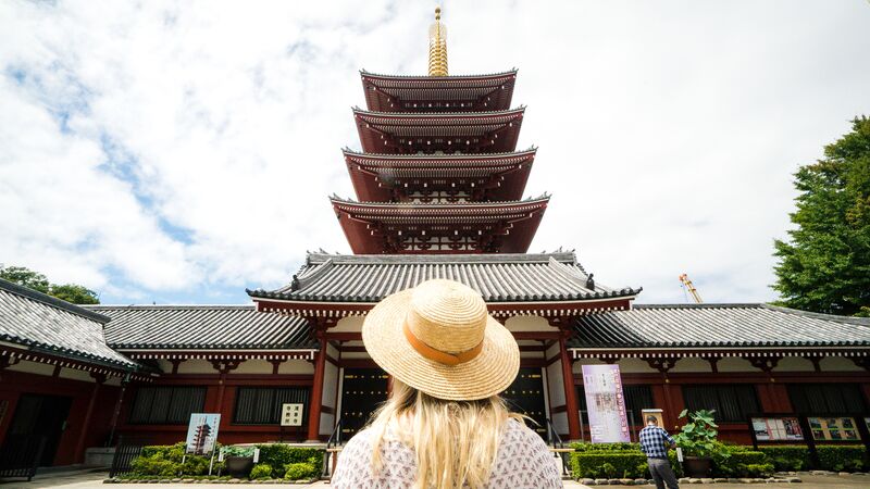 A girl wearing a straw hat in front of a temple in Japan