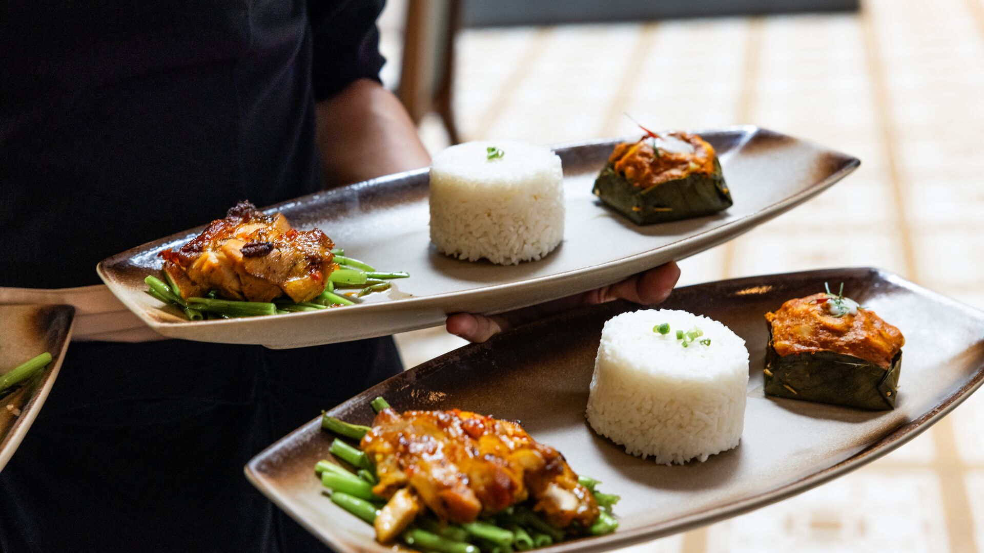 A server holding two dishes filled with green vegetables, chicken and rice. 