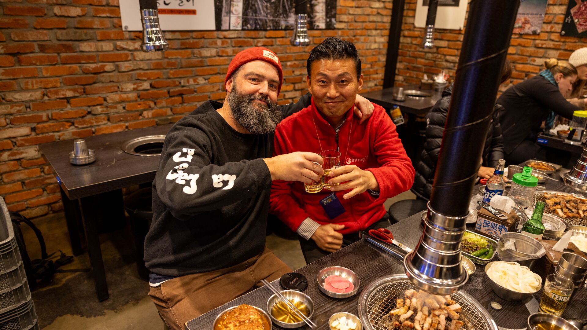 A traveller and a local Intrepid leader pose at dinner as they clink their drinks in South Korea. 