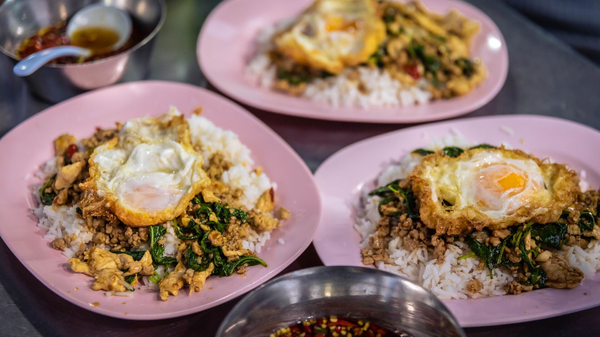 Three dishes with rice, chicken, spinach and egg on a table in Thailand. 
