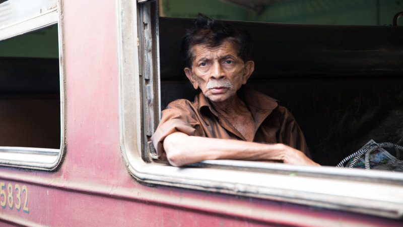 An old man stares out of the window on the train. 