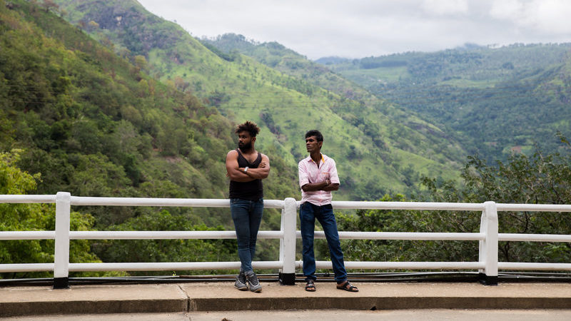 Two men stand on the side of the road. 