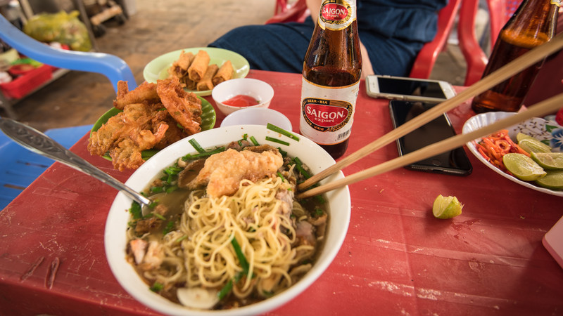 A bowl of noodle soup and a Saigon beer on a street food table in Ho Chi Minh City, Vietnam