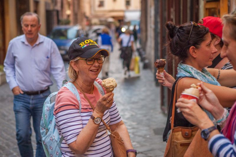 A traveller looking lovingly at a cone of gelato. Her shirt is blue and pink and she wears a hat that says Rome.