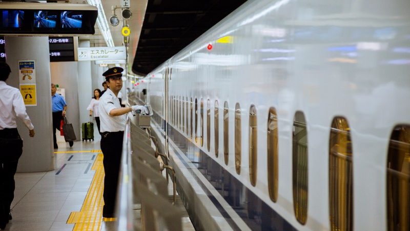 A station attendant stands on the platform at a busy train station in Japan