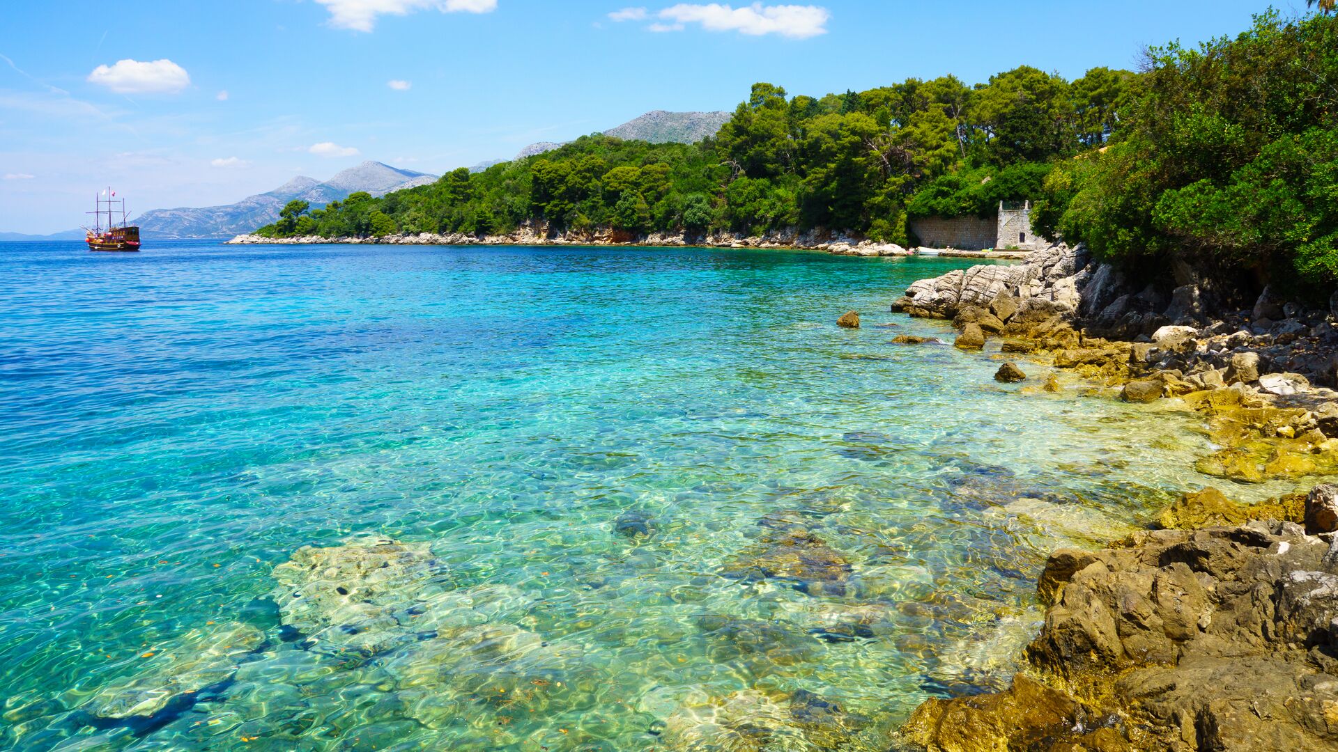 Bright blue and green water on rocky coastal shore with boat in distance