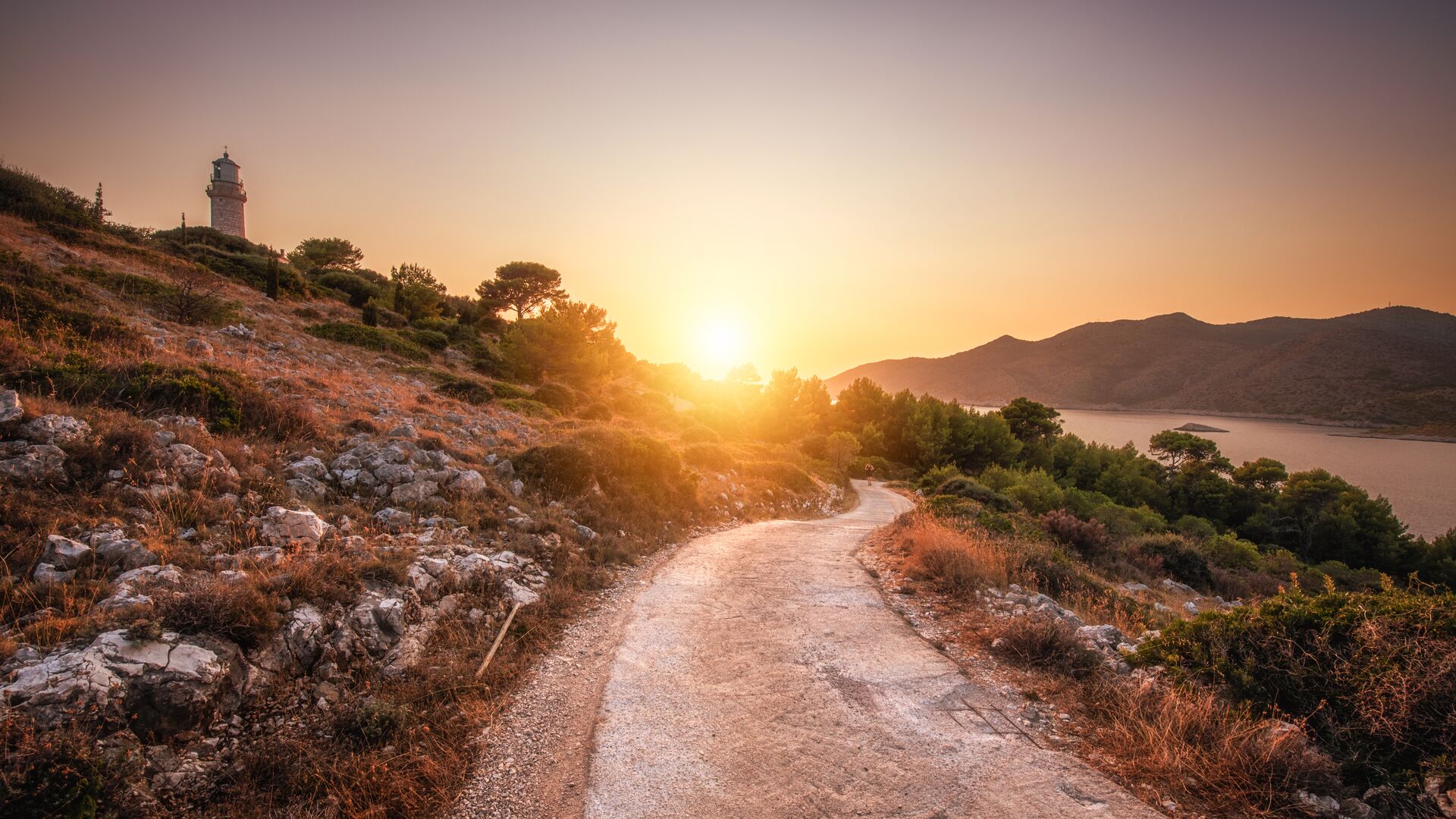 Pathway leading into the hills at sunset, the ocean on one side and a lighthouse in the distance
