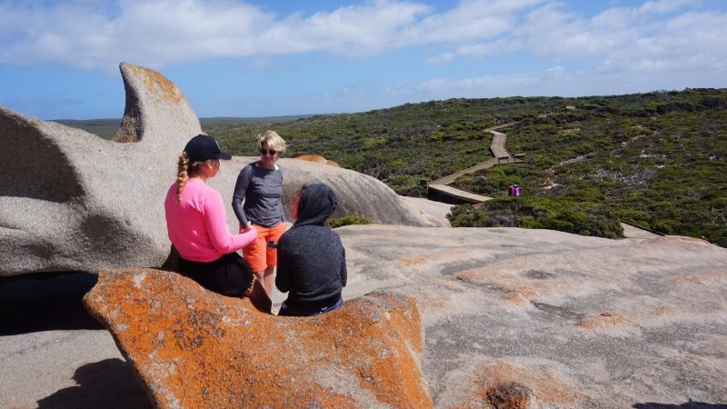 Three woman chat on top of a big rock n Australia