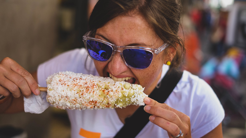 A young women bites into a cob of corn