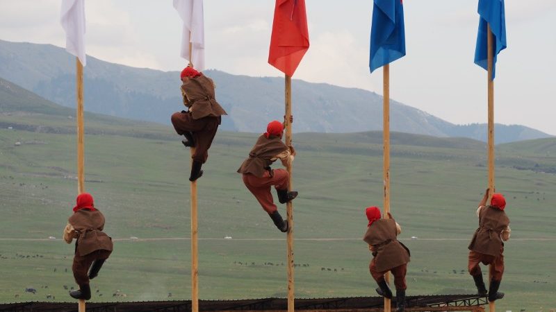 Five competitors climb flagpoles at the World Nomad Games