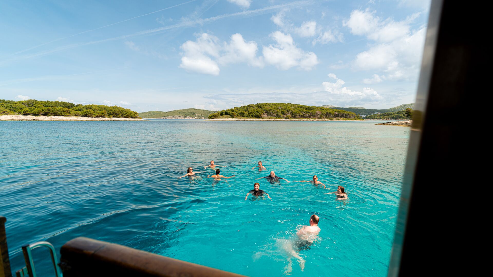 People swim in bright blue water next to a boat