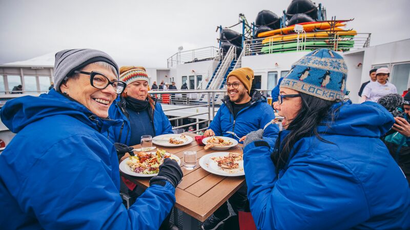 A group of travellers in blue jackets eating on the deck of a ship in Antarctica