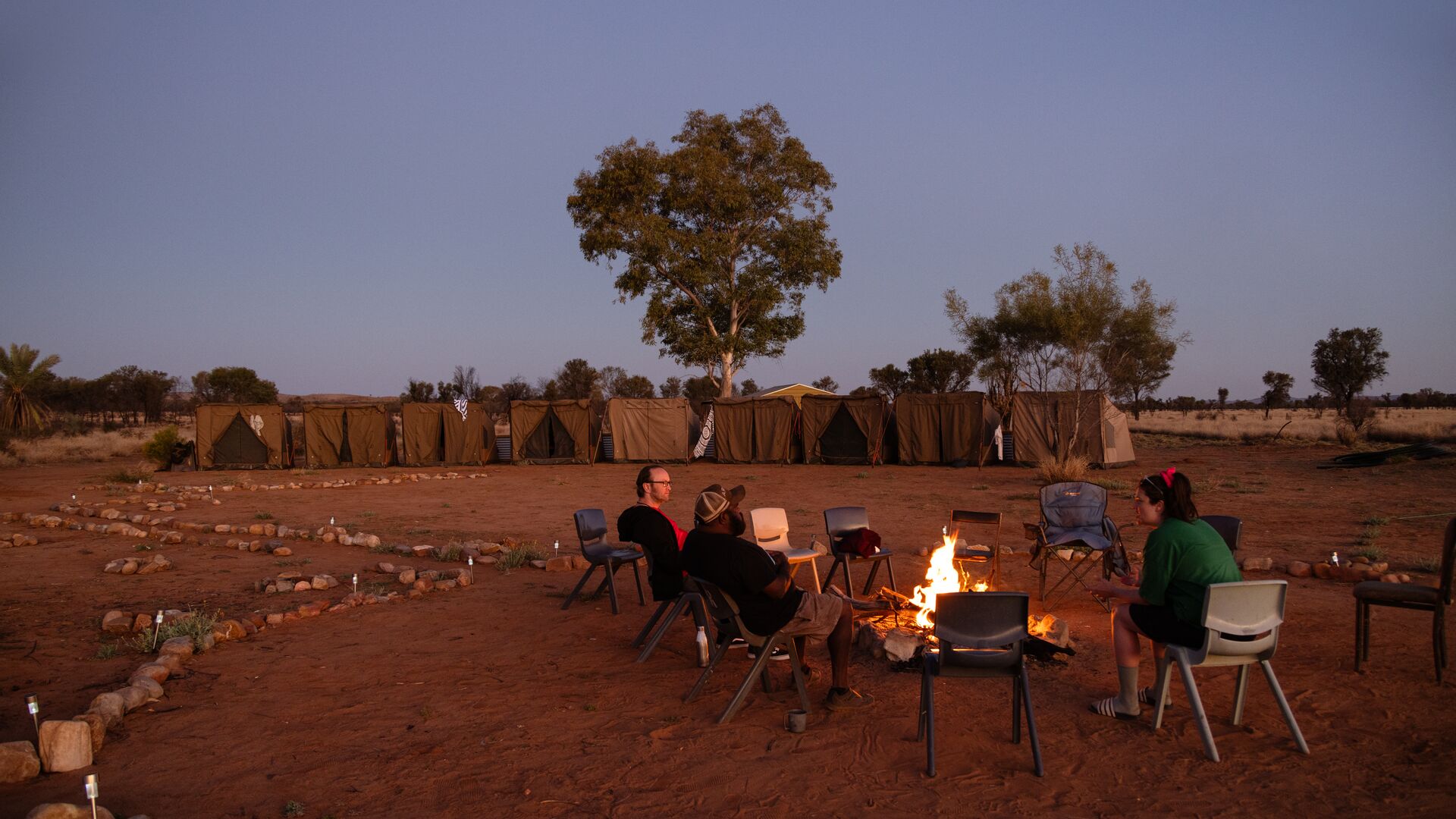 People sit around a campfire with tents in the background during sunset in Rodna
