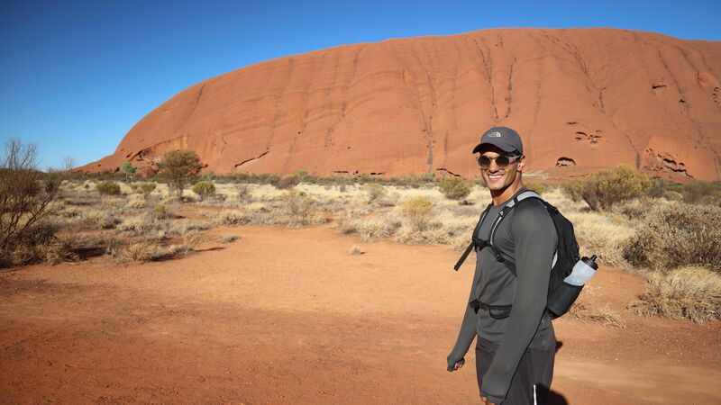 Man smiling in front of Uluru on a walk around the base