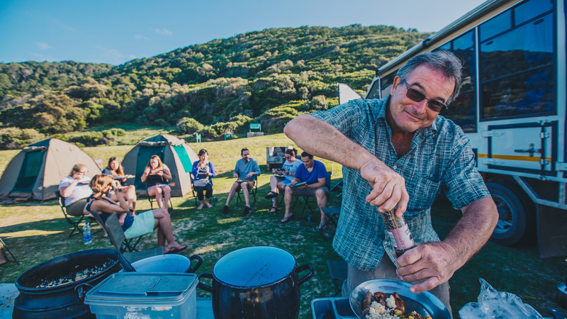 Group of travellers eating dinner at campsite