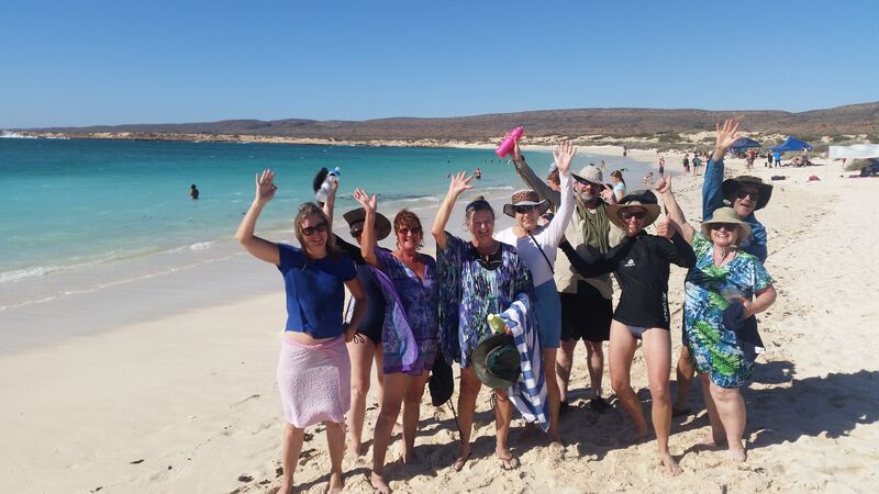 A group of travellers smiling and waving at the camera at Ningaloo Reef