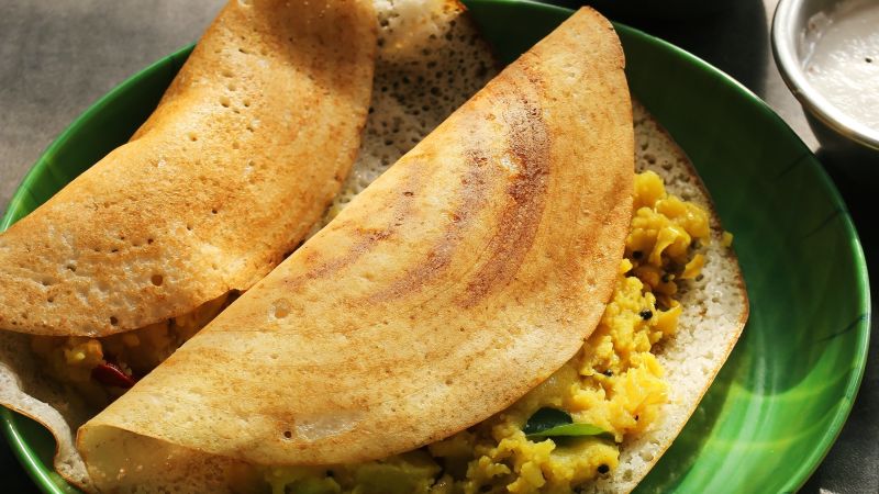 Two dosas filled with curry on a green plate