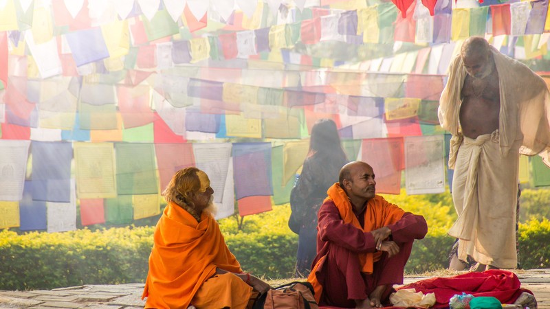 Three sadhus sit under colourful prayer flags