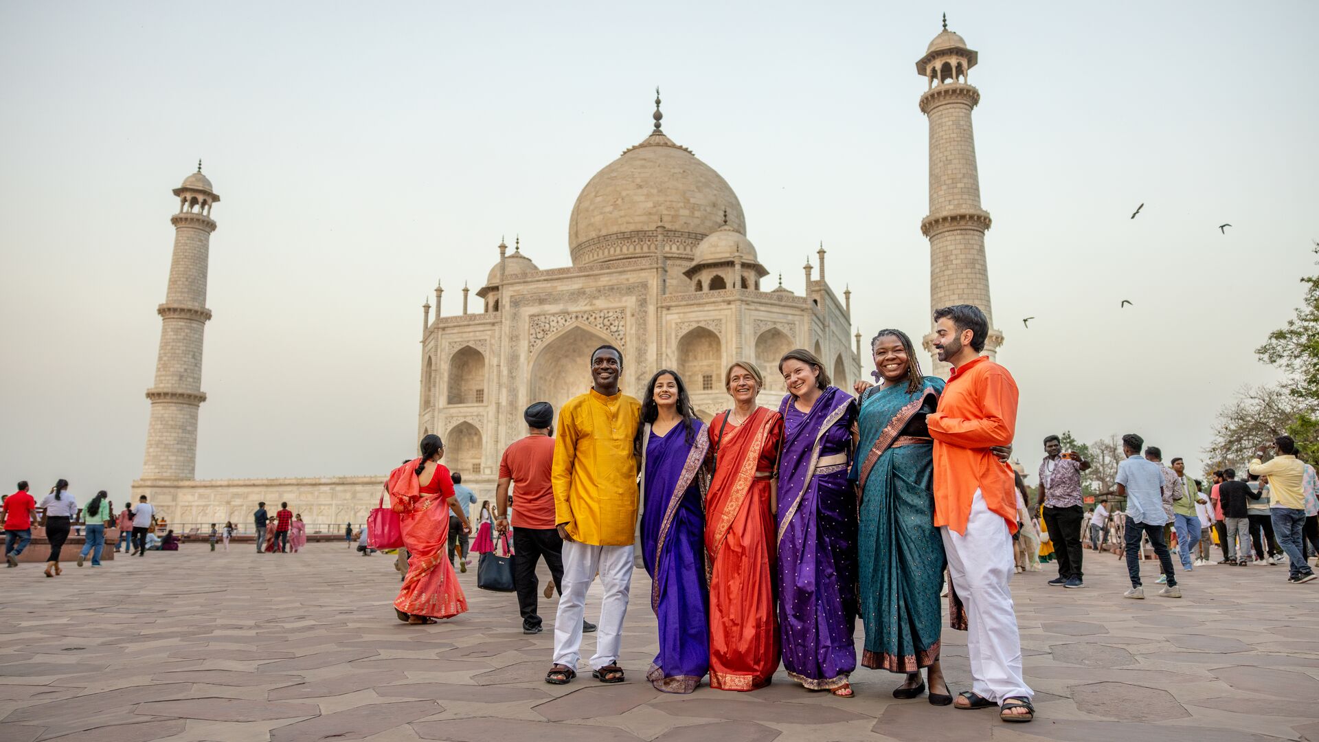 A group of travellers in colourful traditional clothing standing in front of the Taj Mahal. 