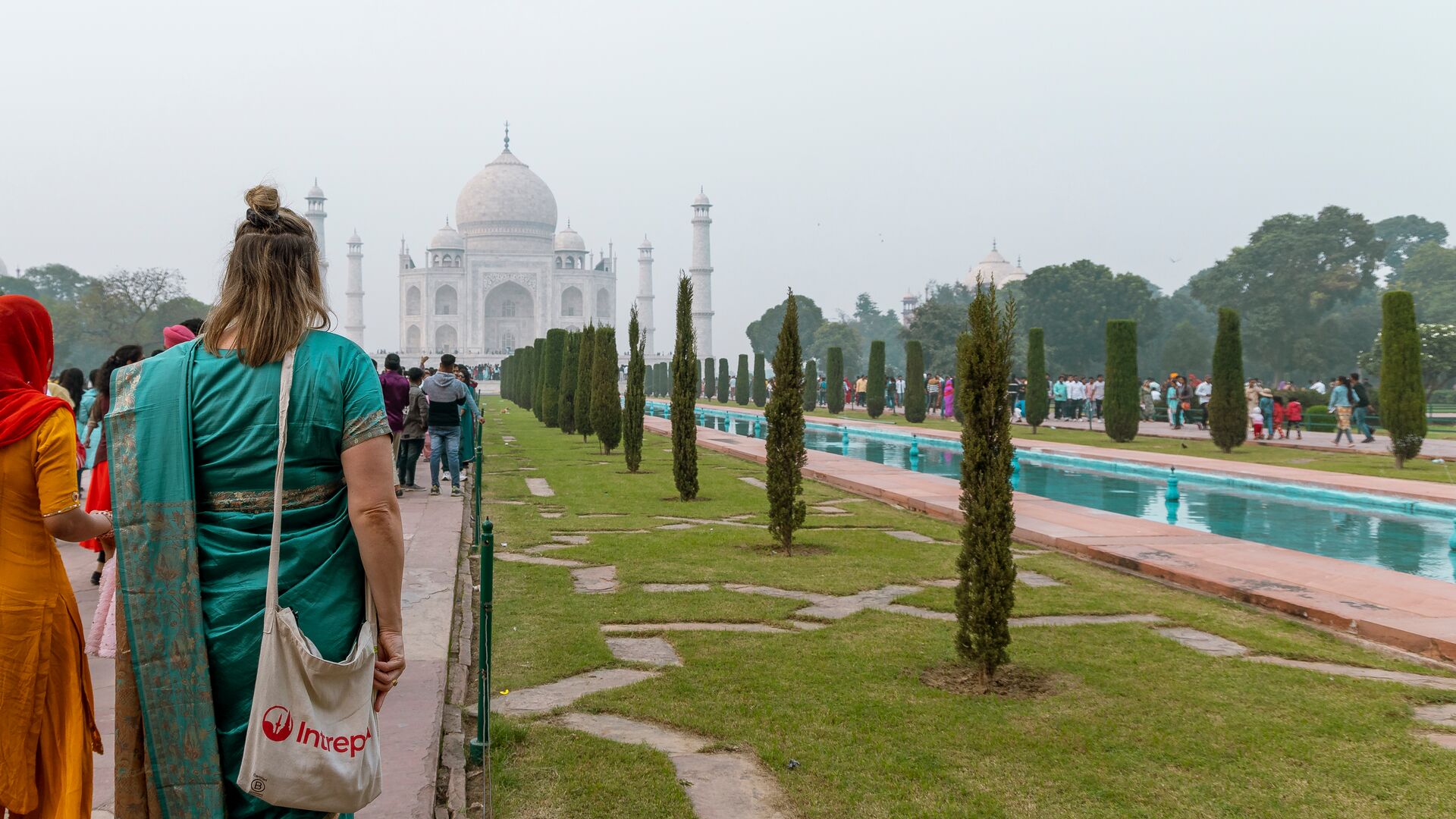 A traveller in a teal-coloured saree stands facing the Taj Mahal in India with an Intrepid tote bag.