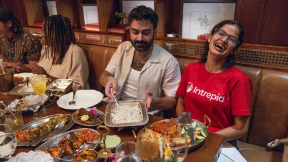 A local leader laughing next to a traveller at a group dinner with a table filled with various food dishes.