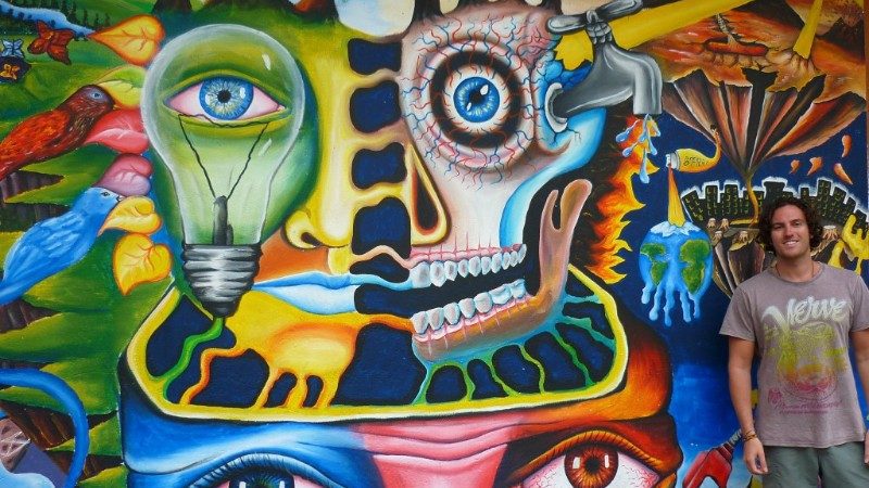 Man poses in front of street art in Banos