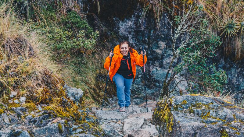 A female hiker in an orange jacket climbing up some stairs on the Inca Trail