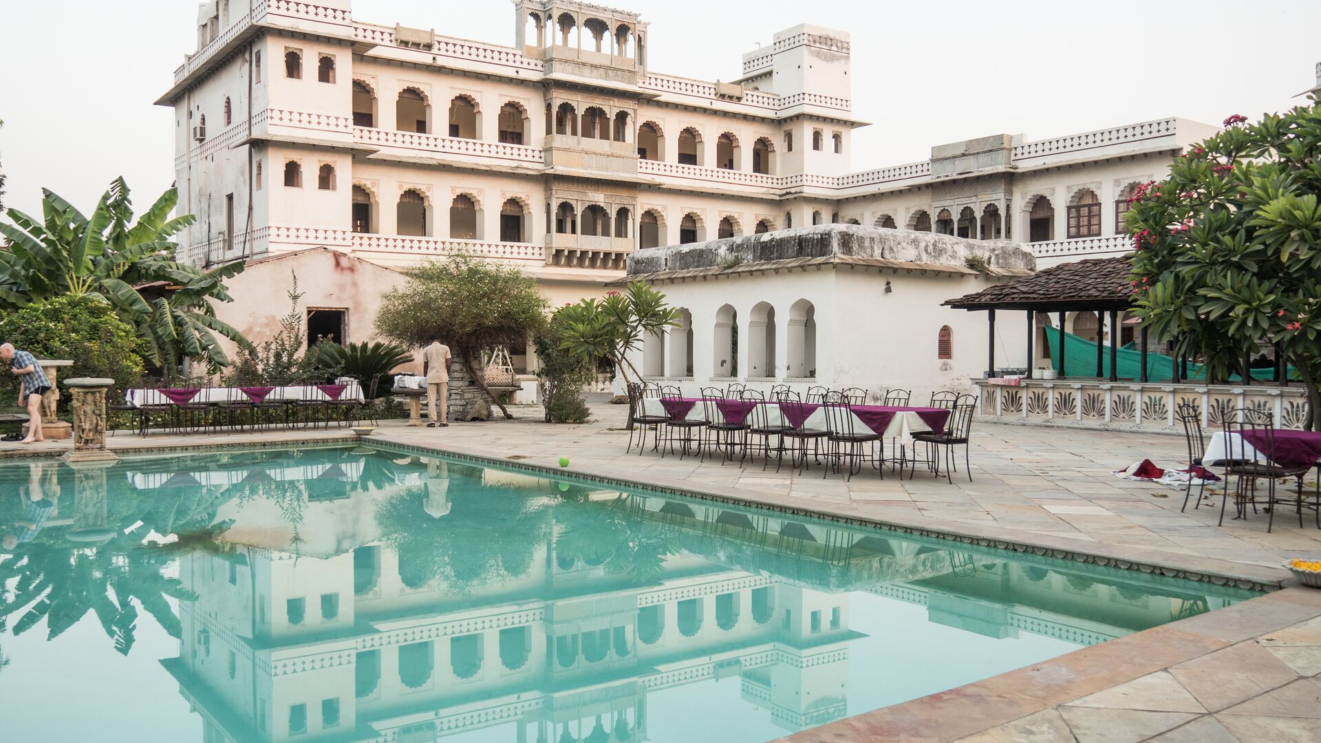 A white heritage property in India with a pool and outdoor tables.