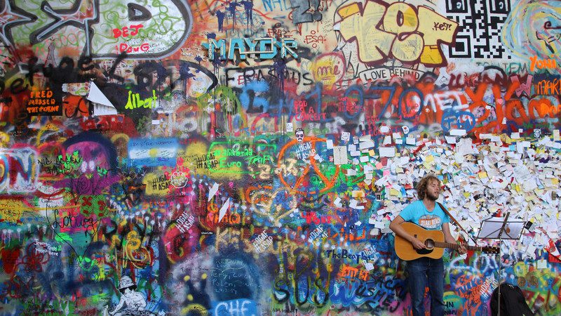 A singer with a guitar performing at the graffiti-laden Wall of Lennon, 