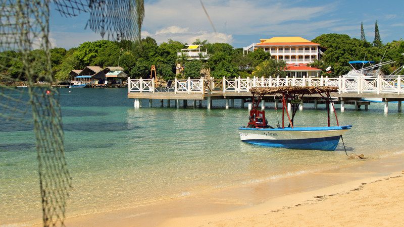 A boat in shallow clear water surrounded by a pier and oceanfront properties, Honduras