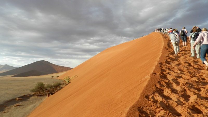 Trekker hike up a sand dune