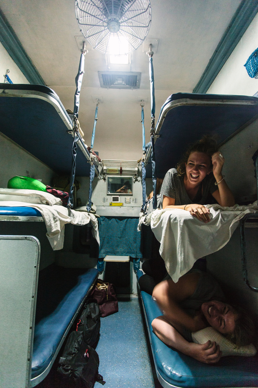 Two female travellers smiling from their middle and bottom bunks on an overnight Indian sleeper train