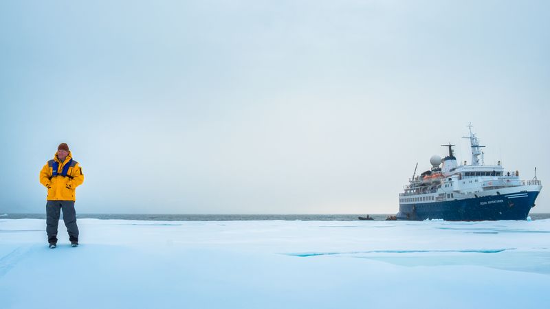 A traveller stands on the ice with a ship in the background