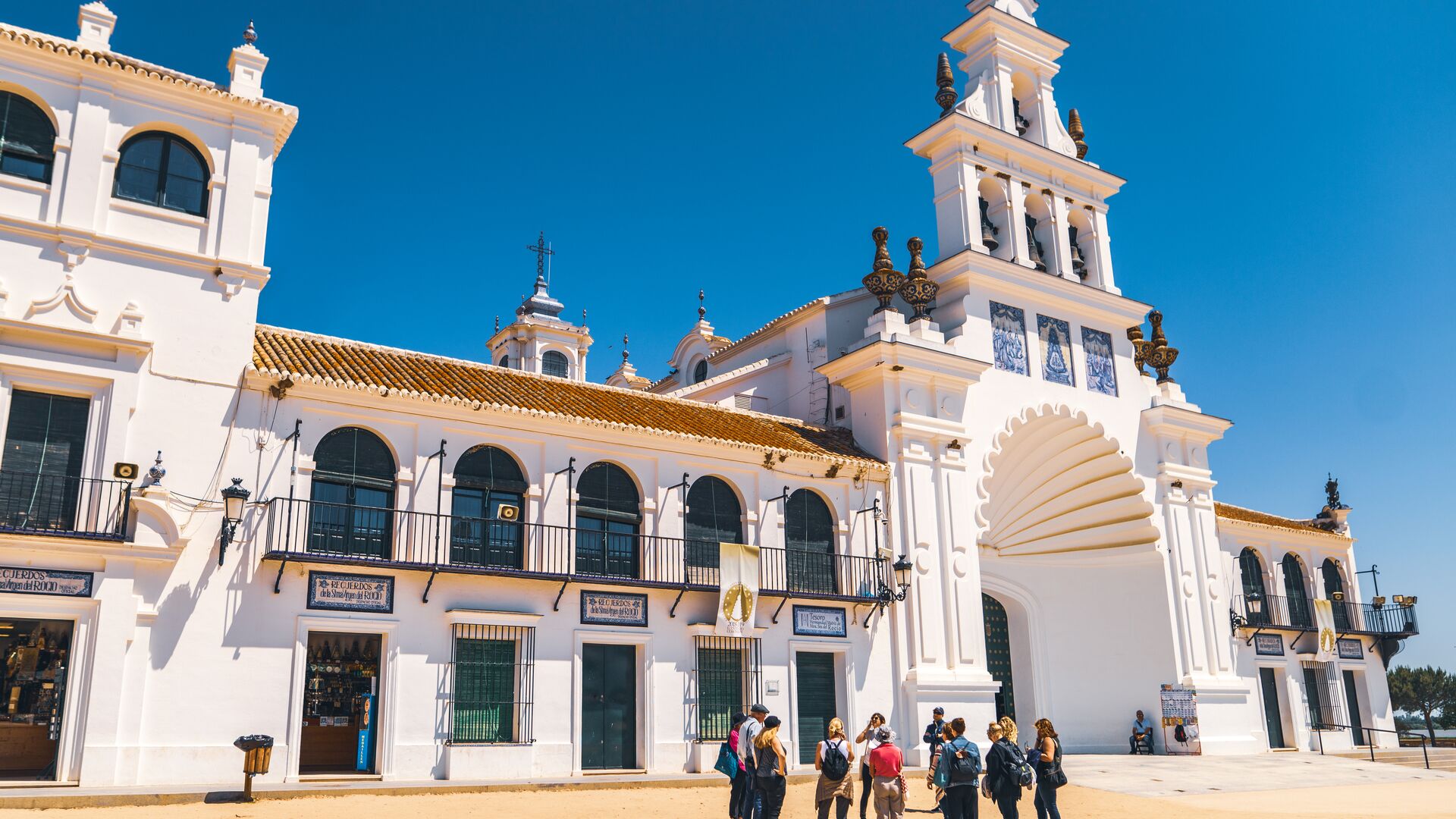 A group of travellers standing in front of the giant white building of the Hermitage of El Rocio in Andalusia, Spain, with a big blue sky.