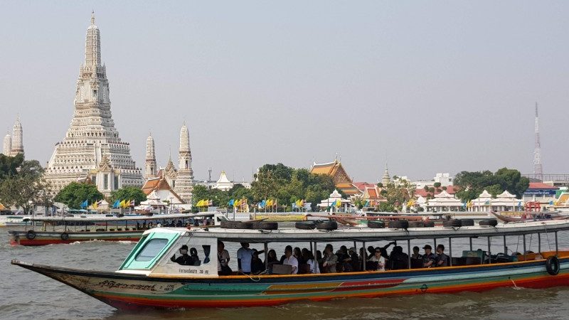 A long boat cruising past a temple in Bangkok