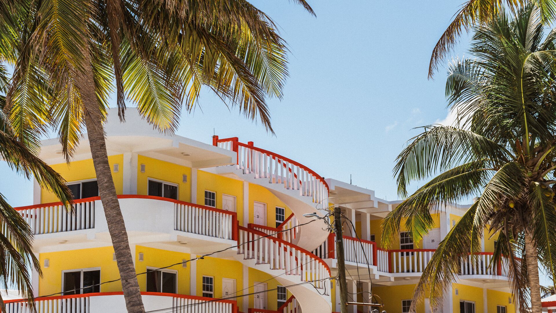 A colourful yellow building in Belize surrounded by palm trees.