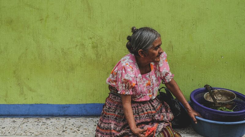 An older woman sitting against a green wall