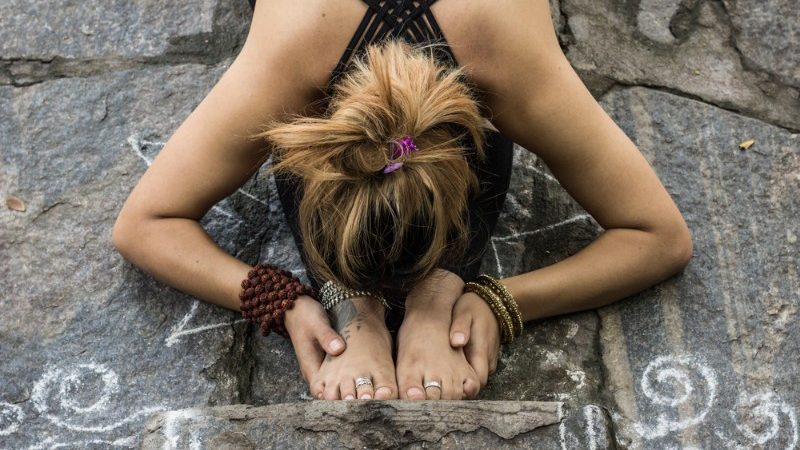 Girl practices a forward bend yoga pose on a stone floor