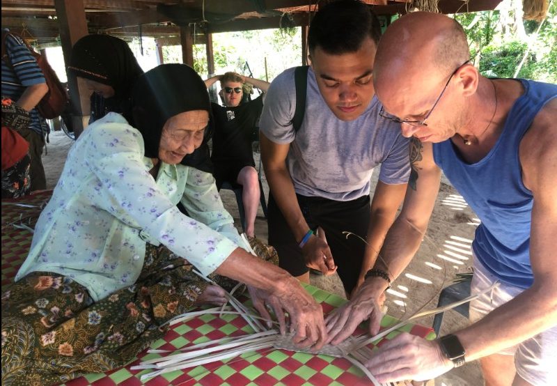An old Thai woman teaching travellers how to weave