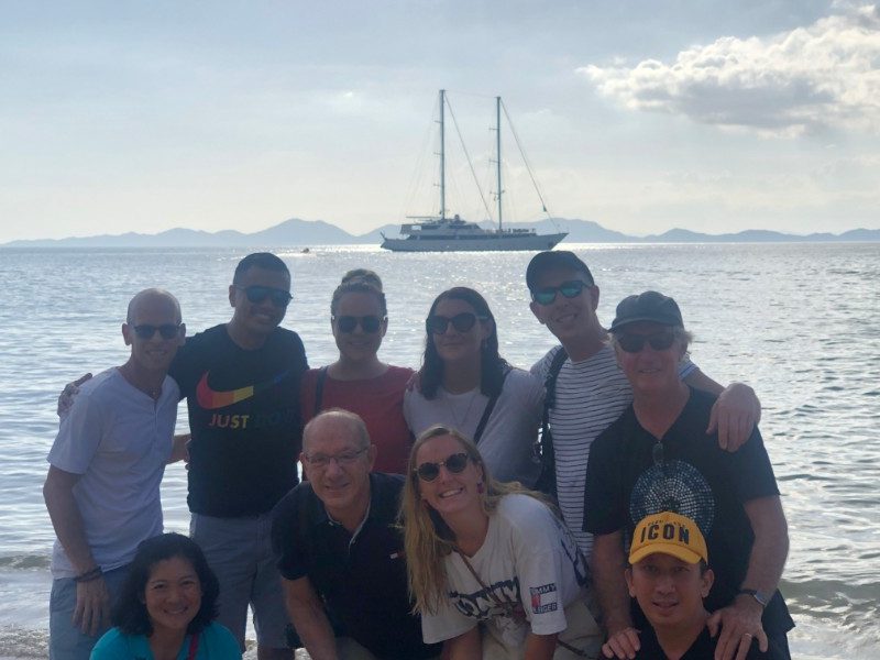 Group photo of travellers with a sailboat in the background