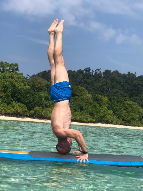 A man does a headstand on a standup paddle board