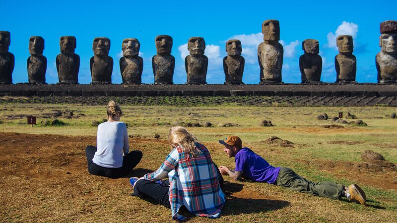 Three travellers sitting in front of the giant stone heads on Easter Island