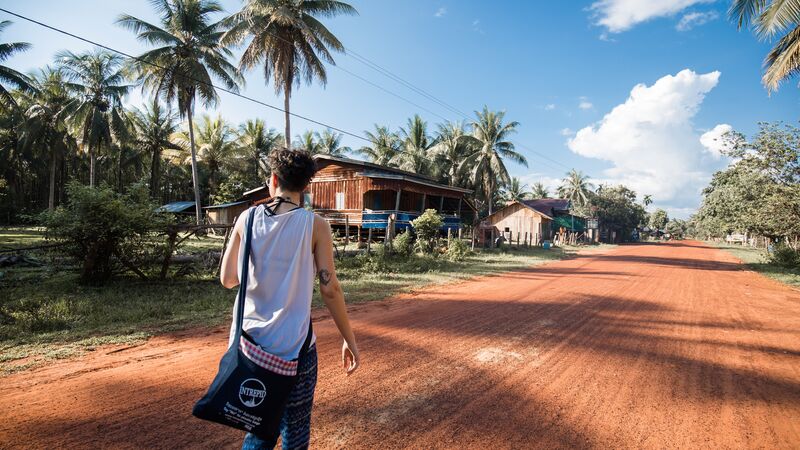 A traveller walks along a dirt road in Cambodia