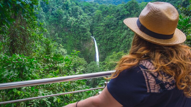 A woman looks over the treetops to a waterfall in Costa Rica