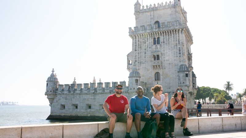 Three travellers and a tour leader sit in front of a castle in Portugal