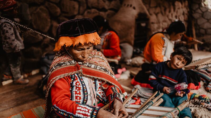 A Peruvian woman weaves while a small child looks on.