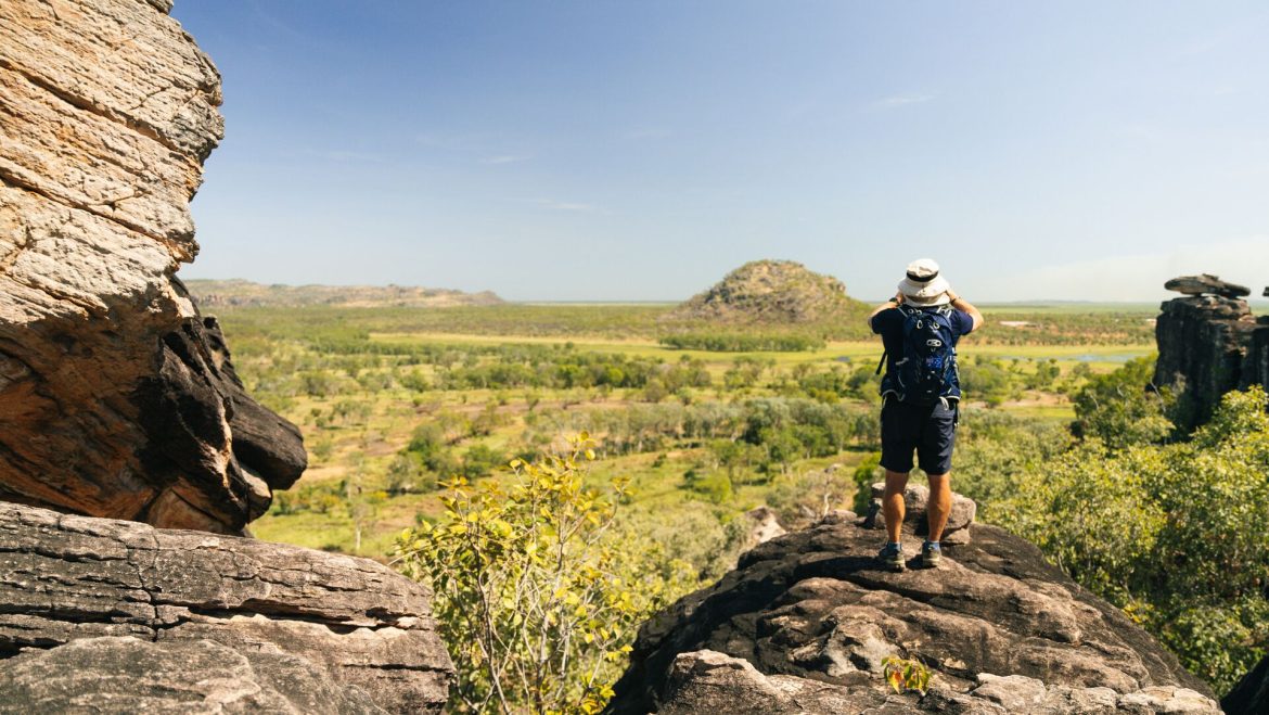 A man stands taking a photo on a rocky ledge in Injalak Hill, Arnhem Land