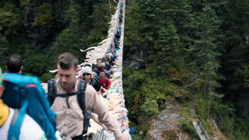 Group of travellers walking along a suspended bridge to Everest Base Camp though forests and shrubs 